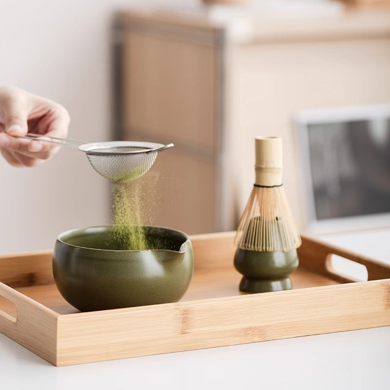 Sifting matcha into a dark green ceramic bowl from the Kumora Ritual Kit