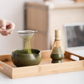 Sifting matcha into the Kumora Ritual Kit's dark green ceramic bowl
