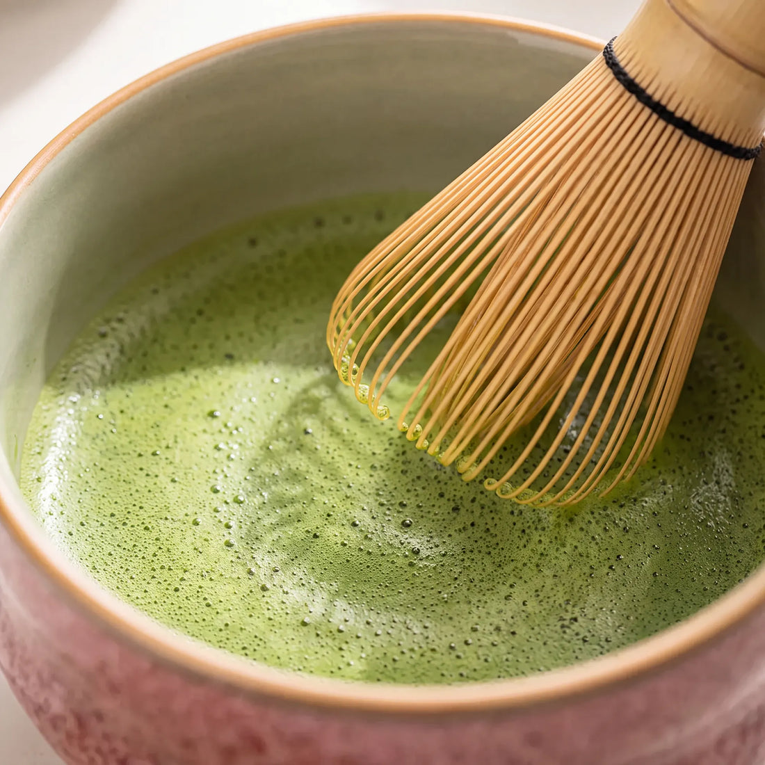 Overhead close-up of a bamboo chasen whisking matcha to a fine foam
