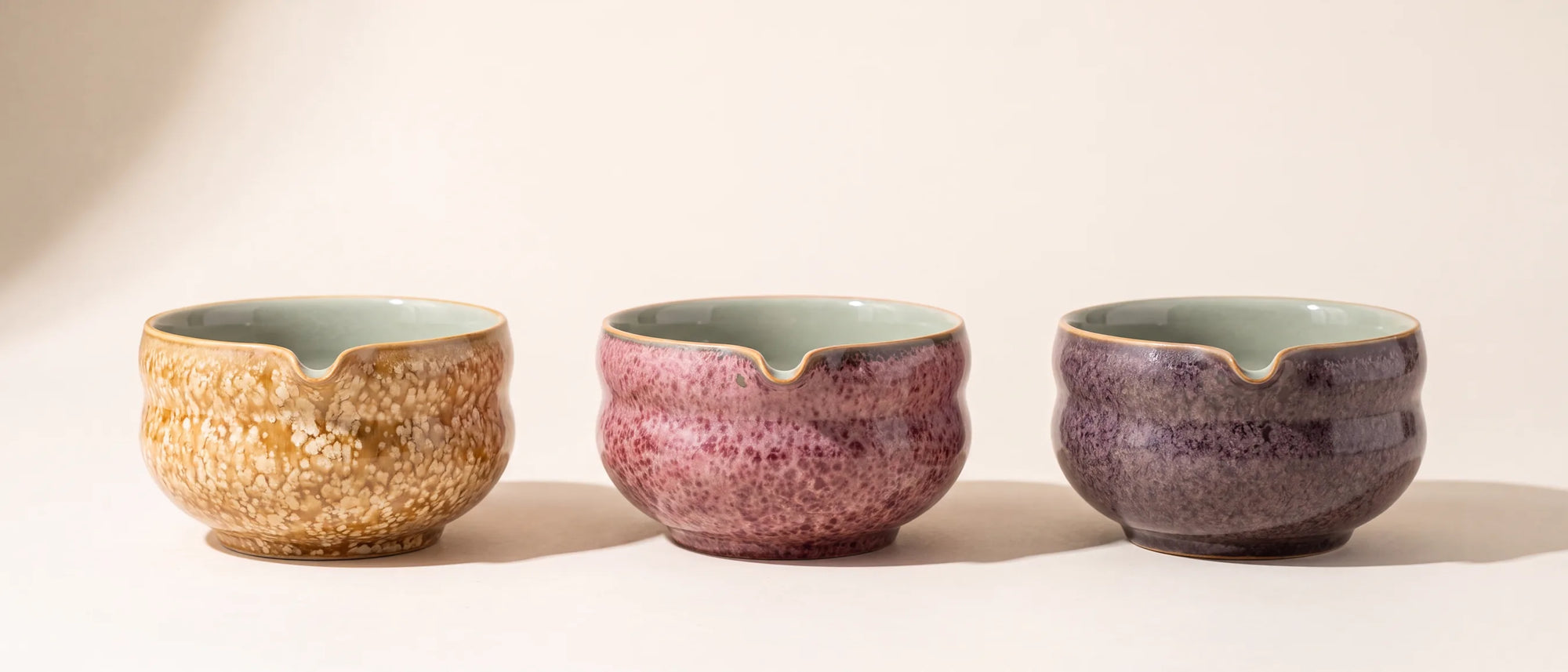 The Kumora matcha bowl in three crystalline glazes — Amber, Ash Rose and Aubergine