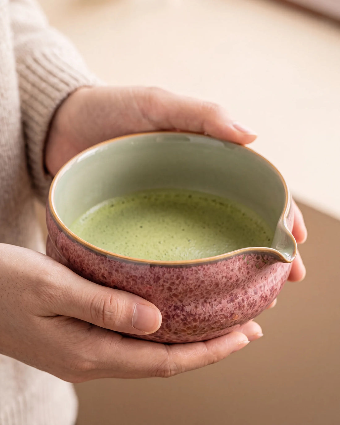 Hands cradling the Kumora matcha bowl in Ash Rose, filled with whisked matcha