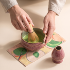 Kumora 7-piece matcha set in Ash Rose — hands whisking bright green matcha to foam in the spouted bowl