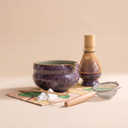 Kumora 7-piece matcha set in Aubergine — straight-on front view, spouted bowl in profile beside the whisk on its stand