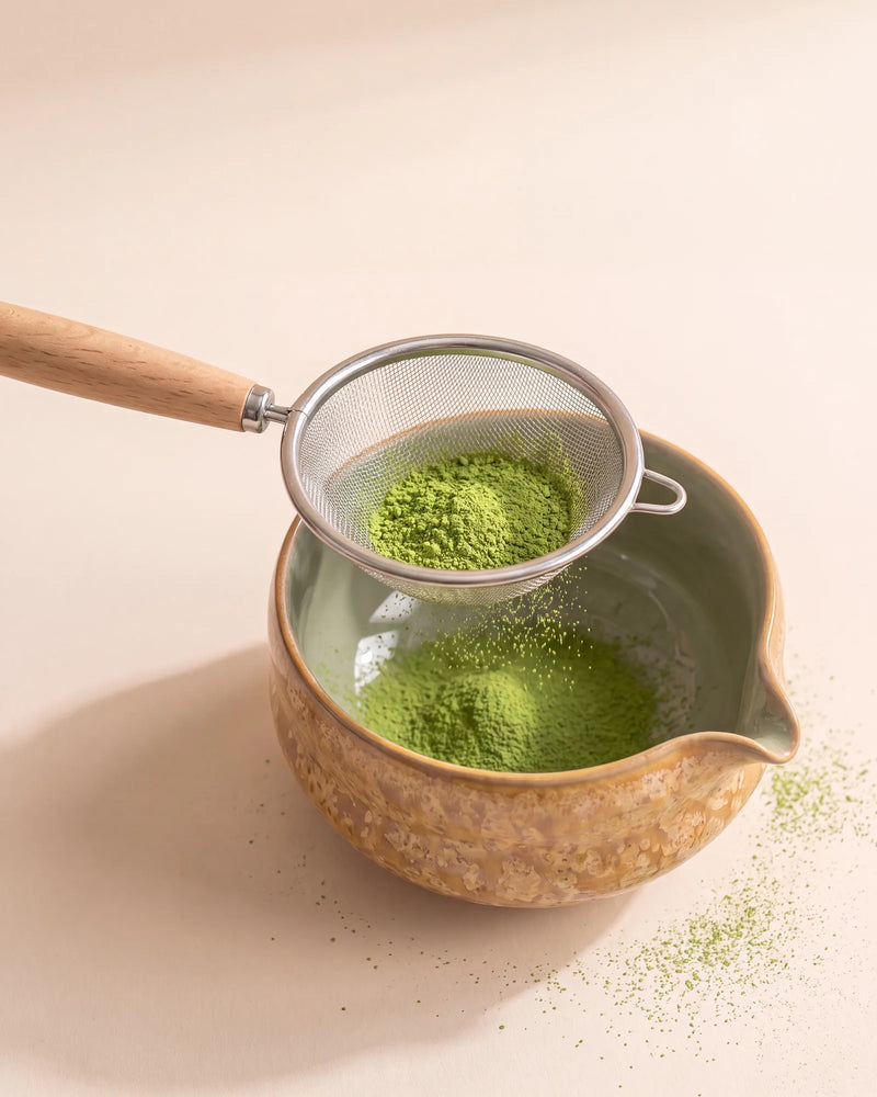 Matcha powder sifted through a steel mesh sifter into the Kumora amber ceramic matcha bowl