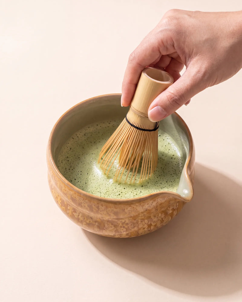 Whisking matcha to a fine foam with a bamboo chasen in the Kumora amber matcha bowl